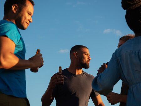 Bottom view of relaxed people standing with beer bottles. Group of friends relaxing in park during...
