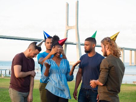 Smiling friends congratulating young woman with birthday. Cheerful young people giving muffin with sparkler. Concept of birthday partyの写真素材