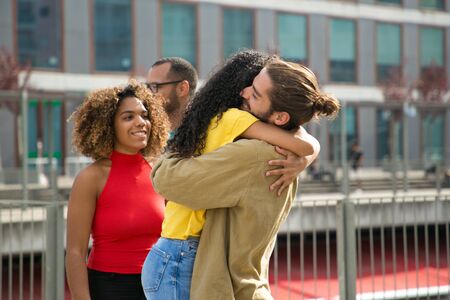 Interracial team of friends meeting and hugging outside. Man and woman standing on outdoor building terrace, embracing and greeting each other. Happy meeting conceptの写真素材