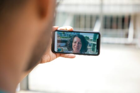 Speaking woman on mobile phone screen communicating through video call. Man holding smartphone and...