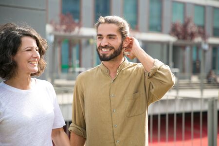 Happy couple of friends enjoying meeting outside. Cheerful Caucasian man and woman standing on outdoor terrace, looking away, smiling, laughing. Friendship and joy conceptの写真素材
