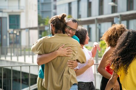 Cheerful male friends hugging each other. Close mix raced friends meeting on outdoor building terrace, embracing and greeting each other. Close friendship conceptの写真素材