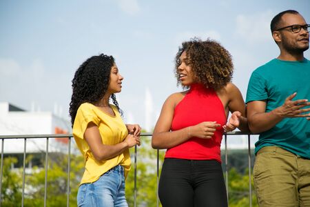 Friendly joyful female friends chatting outside. Young black women standing on bridge outdoors,...