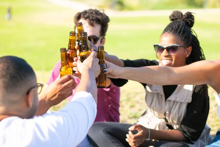 Smiling friends clinking beer bottles during holiday. Group of young people relaxing during sunny day. Leisure conceptの写真素材