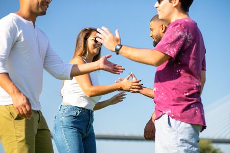 Happy friends standing on meadow and giving high five. Smiling young people having fun in park....