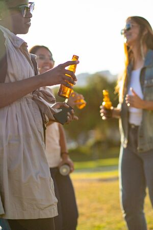 Cropped shot of happy women dancing in park in evening. Cheerful friends relaxing with beer during sunset. Leisure conceptの写真素材
