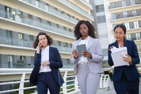 Serious businesswomen with gadgets and papers. Multiethnic female colleagues, holding documents, talking by smartphone and using digital tablet on street. Business conceptの写真素材