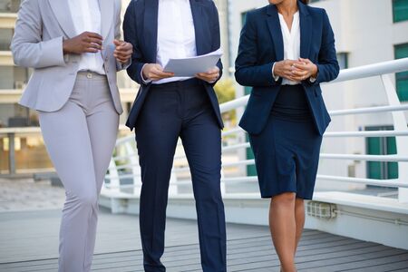 Cropped shot of businesswomen walking on street. Partial view of multiethnic female colleagues in formal wear holding papers and walking outdoor. Cooperation conceptの写真素材