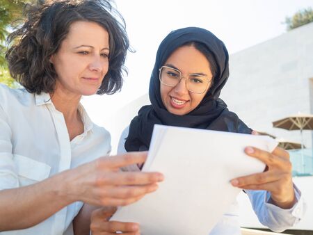 Positive focused female coworkers reviewing paper reports. Multicultural businesswomen in office...