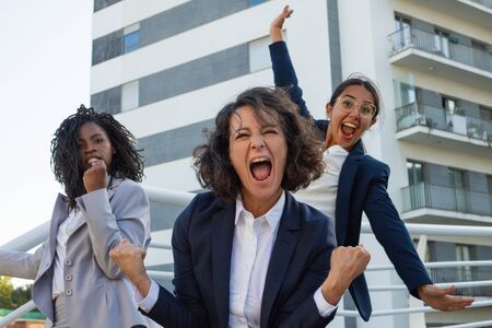 Excited businesswomen triumphing on street. Emotional multiethnic female colleagues yelling and celebrating success outdoor. Business success conceptの写真素材