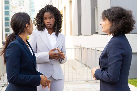 Focused women talking while standing near office building. Confident managers wearing suits communicating outdoor. Business confidence conceptの写真素材
