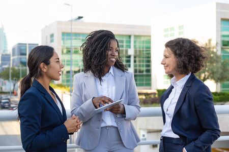 Smiling businesswomen with tablet pc. Cheerful multiethnic female colleagues standing together and using digital tablet on street. Technology conceptの写真素材