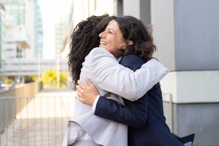 Two smiling businesswomen hugging on street. Cheerful female friends meeting during break. Communication conceptの写真素材
