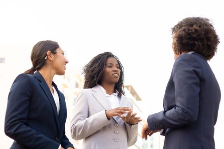 Closeup shot of three business people talking on street. Cropped shot of smiling women meeting outdoor. Business handshake concept