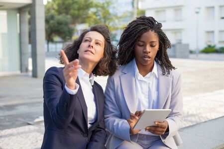 Multiethnic coworkers with tablet pc. Professional multiethnic businesswomen sitting outdoor and...