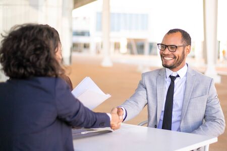 Successful business people meeting outside and closing deal. Happy business man and woman sitting at table, talking and shaking hands. Deal or success conceptの写真素材