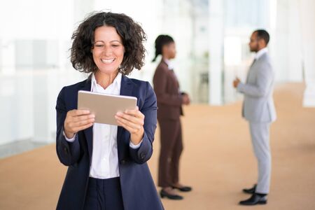 Happy businesswoman watching funny videos or using tablet for video call. Business woman with tablet standing in hallway, looking at screen, smiling, laughing. Happy tablet user conceptの写真素材