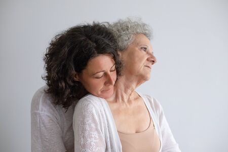 Middle aged daughter hugging senior mother. Pensive adult daughter embracing elderly mother isolated on grey background. Togetherness conceptの写真素材
