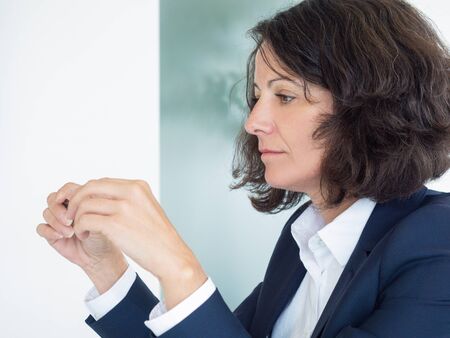 Side portrait of sad, pensive female office employee. Business woman sitting at table indoors, holding and looking at pen. Mistake conceptの写真素材