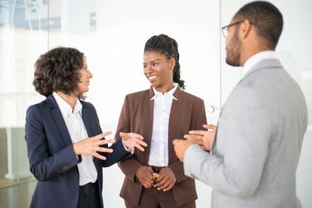 Multiethnic business team discussing project. Business man and women standing in office corridor, talking, gesturing, chatting, laughing. Corporate meeting conceptの写真素材