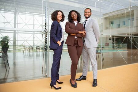 Cheerful multiethnic business team. Full length view of professional businessman and businesswomen standing together and smiling at camera. Teamwork conceptの写真素材