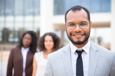 Cheerful African American businessman. Portrait of handsome young businessman smiling at camera while female colleagues standing behind. Leadership conceptの写真素材