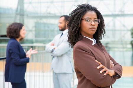 Confident African American businesswoman. Serious young businesswoman standing with crossed arms and looking at camera while colleagues standing behind. Business conceptの写真素材