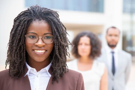 Smiling young African American businesswoman. Portrait of beautiful happy young businesswoman standing with multiethnic colleagues, selective focus. Teamwork conceptの写真素材
