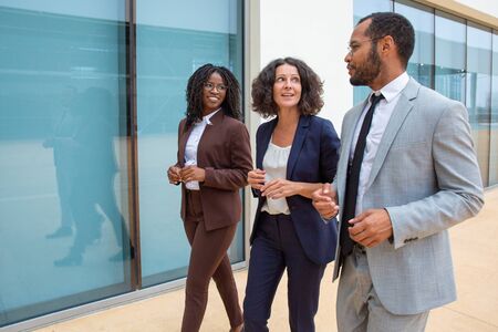 Happy business people walking and talking. Multiethnic male and female business colleagues talking while walking outside office building. Cooperation conceptの写真素材