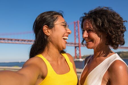 Joyful excited female friends enjoying walk and taking selfie outdoors. Two women standing on city...