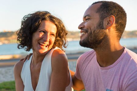 Sweet couple dating outdoors, chatting and having fun. Man and woman sitting on grass, talking and...