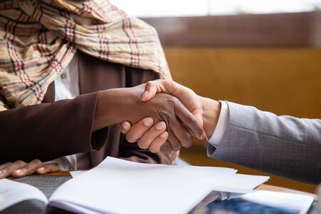 Closeup of businesspeople handshake. Business man and woman in hijab shaking hands with each other over table with documents. Handshake conceptの写真素材