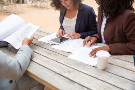 Business partners reading agreement text in street cafe. Business man and woman sitting at table with takeaway coffee, reviewing and studying documents, using tablet. Partners meeting conceptの写真素材