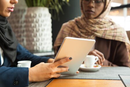 Female colleagues watching content on tablet in coffee shop. Muslim business women in hijabs sitting...