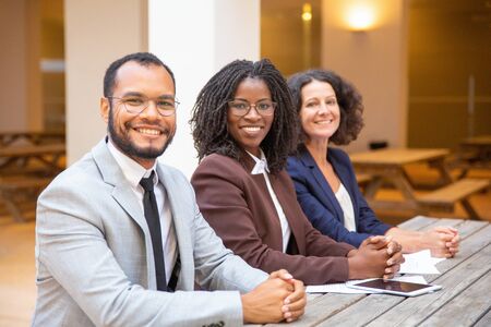 Happy diverse business team posing in street cafe. Business man and women with clasped hands sitting...