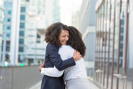 Old female friends glad to see each other outside. Business women standing in city street and hugging. Meeting and joy conceptの写真素材