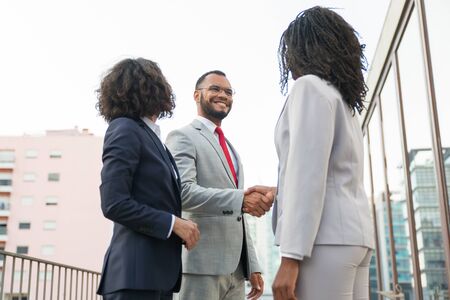 Friendly colleagues greeting each other near office building. Business man and women standing in city street and shaking hands. Corporate communication conceptの写真素材