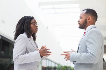 Serious excited business partners arguing about deal in office hall. Business man and woman standing in hallway, talking and gesturing. Negotiation conceptの写真素材