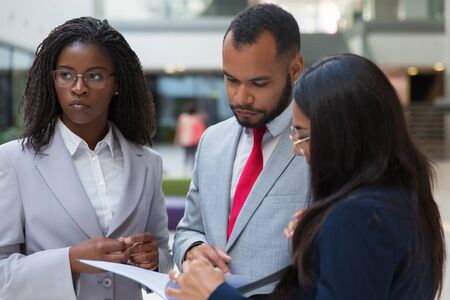 Serious business colleagues with papers. Multiethnic young business people standing together and looking at folder with documents. Business conceptの写真素材