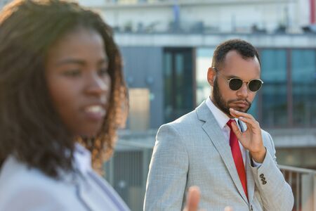 Serious businessman walking outside by his female colleague. Business man in formal suit and sunglasses standing near office building and posing for camera. Businesspeople outside conceptの写真素材