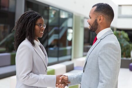 Happy successful business people greeting each other in office hallway. Business man and woman standing and shaking hands. Handshake conceptの写真素材