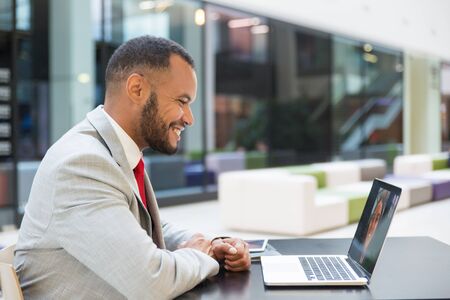 Smiling young businessman chatting via laptop. Cheerful African American businessman using laptop computer and having video chat with colleague at lunchtime. Communication conceptの写真素材