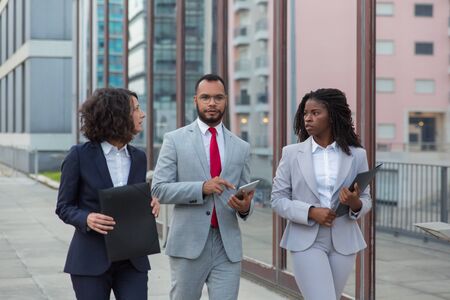 Serious multiethnic business people on street. Professional business colleagues with folders and digital tablet walking together outside office building. Cooperation conceptの写真素材