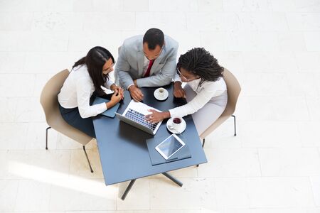 Business colleagues watching content on laptop while drinking coffee. Business man and women sitting at table with tablet, working on computer, looking at screen. Wireless communication conceptの写真素材