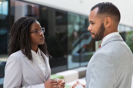 Serious stressed coworkers discussing bad news in office hall. Business man and woman standing in hallway and talking. Corporate relationship conceptの写真素材