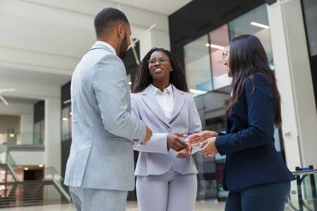 Happy diverse partners discussing deal in office hall. Business man and women standing in hallway, talking and laughing. Business communication conceptの写真素材