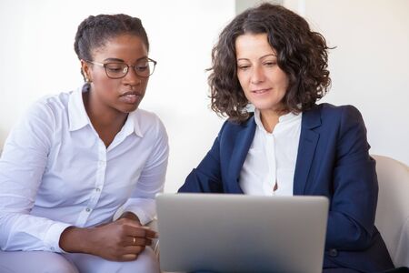 Confident businesswomen discussing project. Business women sitting in armchairs, using computer,...