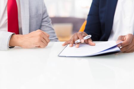 Two business colleagues reading contract. Business man and woman sitting at office table, holding pen and checking documents together. Signing contract conceptの写真素材