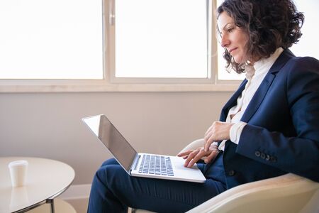 Satisfied business professional working in office lounge. Business woman sitting in armchair and...