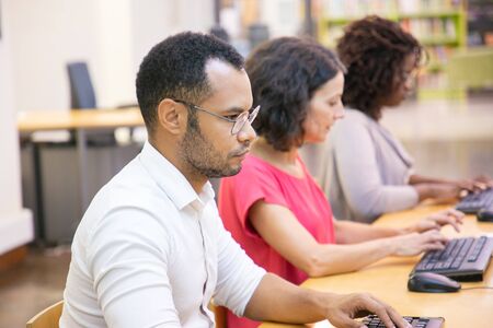 Serious adult male student studying in computer class. Row of man and women in casual sitting at...